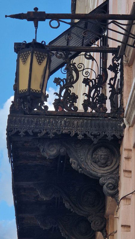 Декоративный кованый балкон и резные элементы фасада старинного дома; деталь городской архитектуры, характерная для центра Ельца.