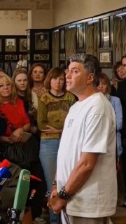 Артист в белой футболке стоит у микрофонов на пресс-подходе, вокруг — журналисты и зрители, происходит интервью.