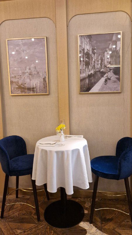 Небольший столик у стены в Garda caffe: белая скатерть, две синие кресла и фотографии в рамках — уютный уголок для завтрака.