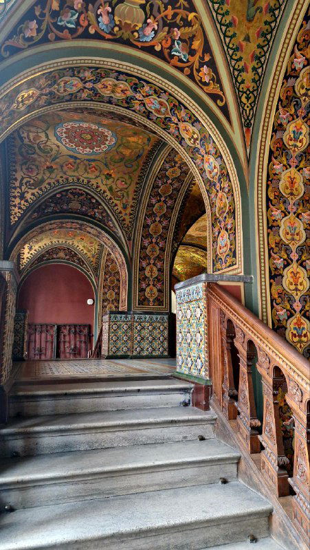 Декорированная лестница Академии Штиглица с богатыми орнаментами и росписями на арках; мозаичные панели и исторический карниз в кадре.