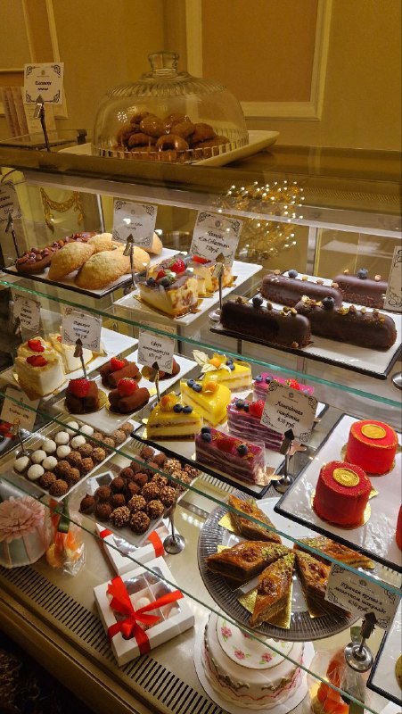 Витрина с десертами и пирожными в кафе: разнообразные торты, мини-десерты и конфеты под стеклом — вкусная кондитерская презентация