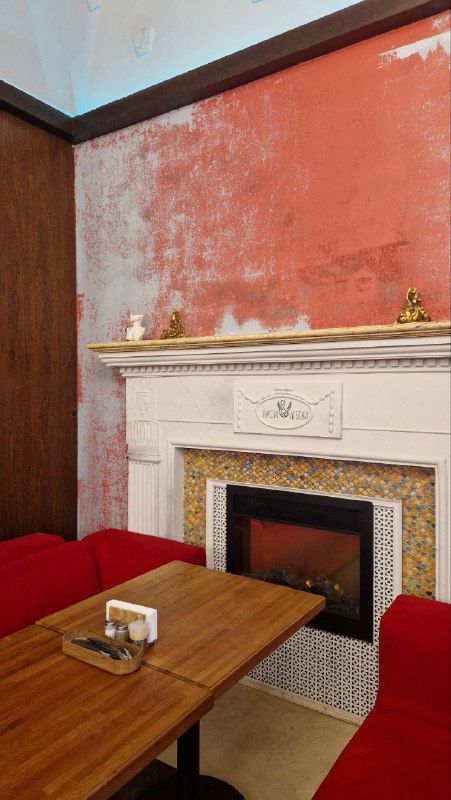 Уютный уголок кафе с красной стеной и камином: диваны, столик и декоративный портал — спокойное место для перекуса на Васильевском