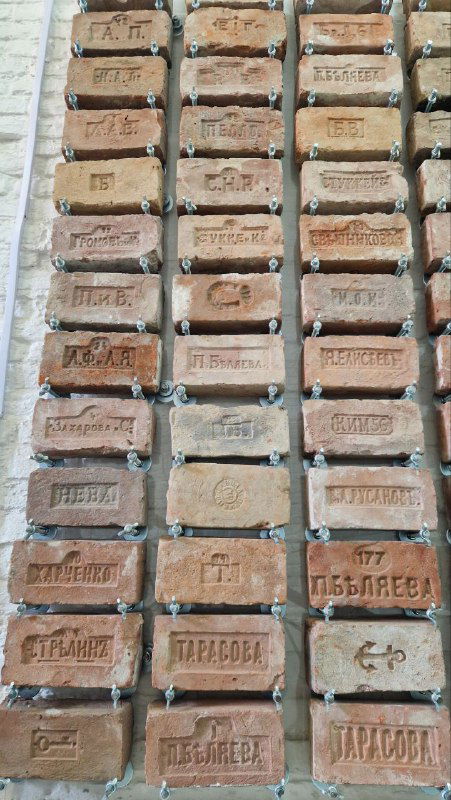 Ряд старинных кирпичей и клейм производителей, выставленных на стенде: примеры кирпичной клеймы и архитектурного материала.