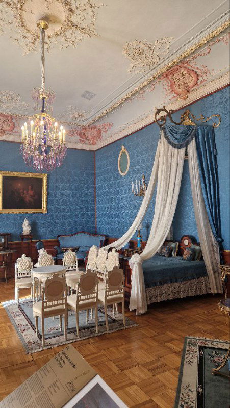 Камерная спальня или гостиная с балдахином над кроватью, синий текстиль, хрустальная люстра и обеденный гарнитур — интерьер для приёма гостей во дворце.