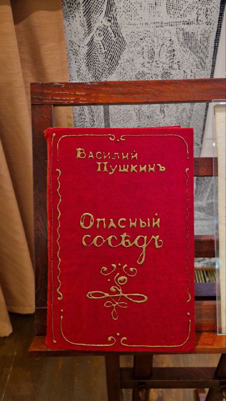 Красная обложка книги Василия Пушкина с заголовком «Опасный сосед» на музейной витрине — экспонат, связанный со скандальной поэмой.