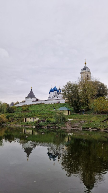Вид на монастырский комплекс и его отражение в спокойной поверхности пруда у Соборной горы в Серпухове, зелёные берега и архитектурные силуэты.