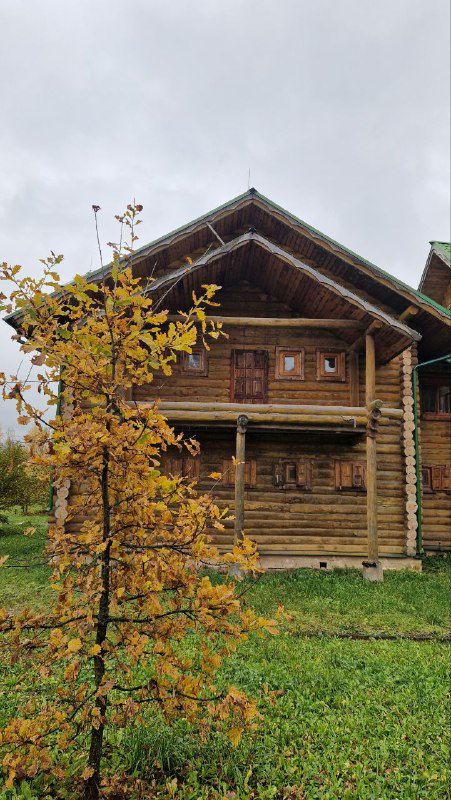 Деревянный двухэтажный дом с резными наличниками и осенним кустом на переднем плане — фасад экспозиционного дома.