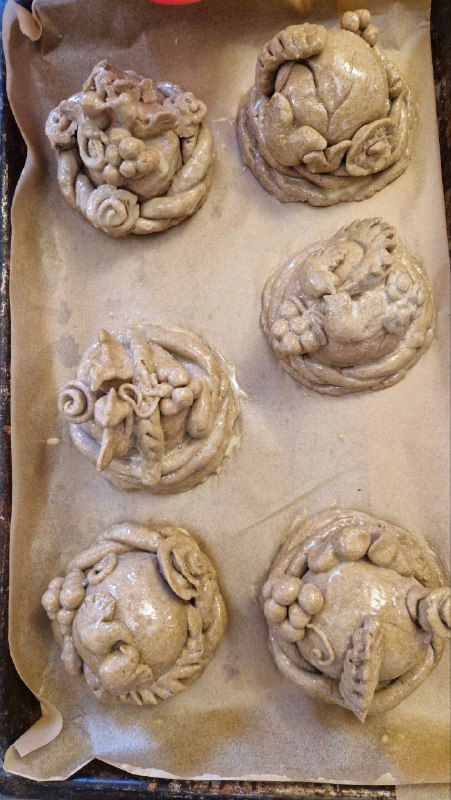 Заготовки из теста с украшениями в виде птиц, колосьев и цветов перед выпечкой караваев — кадр мастер-класса по лепке.