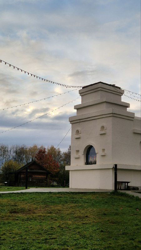 Белая печная труба и часть двора этнографического комплекса на фоне облачного неба — общая сцена территории.