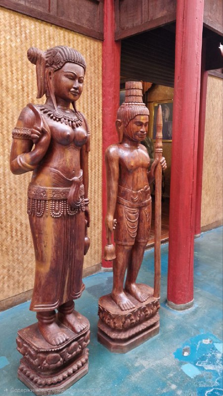 Резные деревянные статуи в этнопавильоне Этномира: женская и мужская фигуры в традиционной азиатской манере, текстура и детали резьбы.