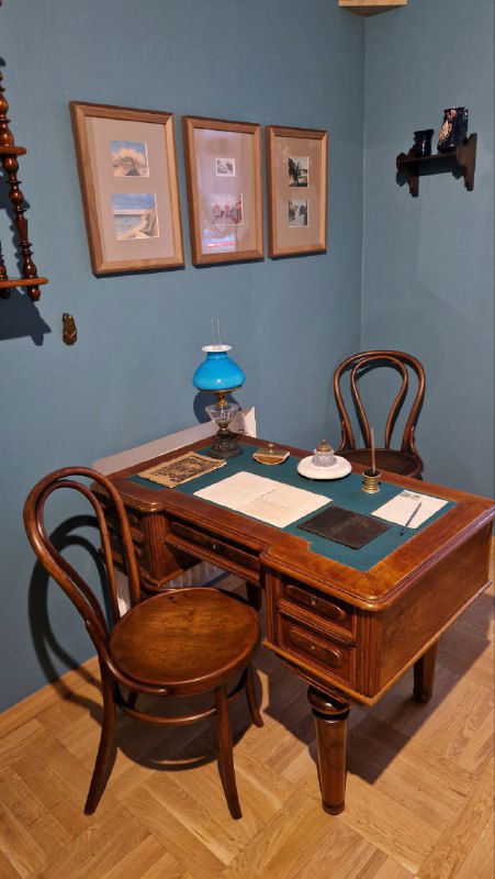 Рабочее место писателя: письменный стол с предметами быта, лампа и канцелярские принадлежности, оформлен как историческая реконструкция
