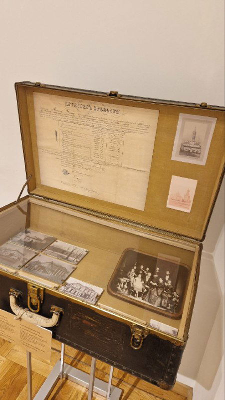 Экспозиция с чемоданом и документами: афиши, фотографии и бумажные носители аккуратно разложены внутри витрины музейного экспозиционного стенда