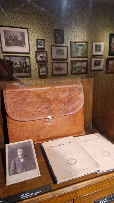 Витрина с предметами быта и печатными изданиями: портфель, книги и фотографии — часть собрания музея Чехова на демонстрационной полке