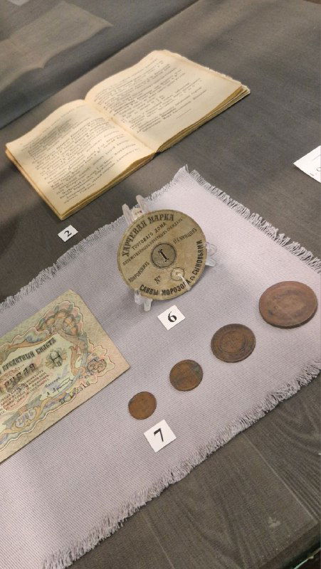 Экспонаты в стеклянном боксе: бумажные харчевые боны и металлические монеты, подписанные номера и музейная подложка с описанием.