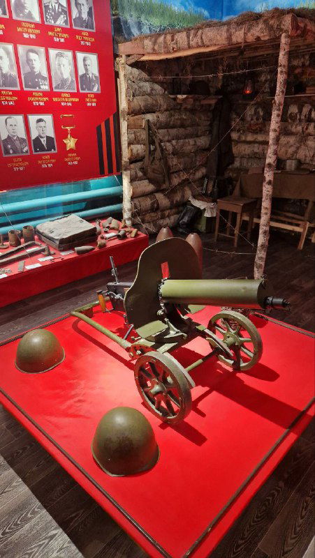 Военно-историческая инсталляция: станковый пулемёт «Максим» на подставке, каски и наградные доски на фоне — зал о войне и памяти.
