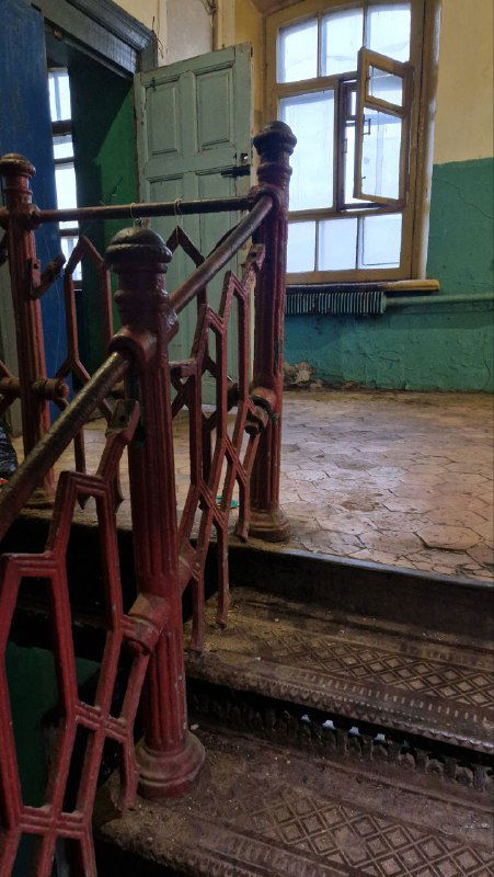Интерьер старой казармы: деревянная или чугунная лестница, потертая плитка и естественное освещение через окно — атмосферный исторический интерьер.