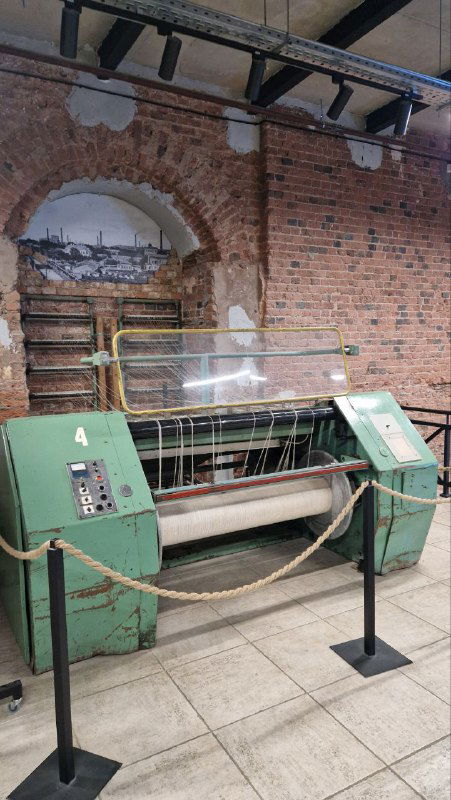Ткацкий станок, выставленный на первом этаже как напоминание об истории фабрики: металлическая машина, ограждение и кирпичные стены вокруг.