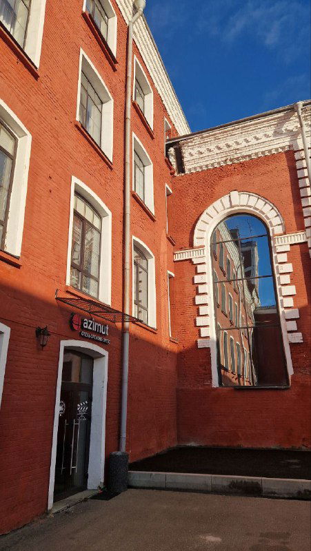 Краснокирпичный фасад или внутренний двор бывшей мануфактуры с аркой и ярким небом — архитектурные детали исторического ансамбля.