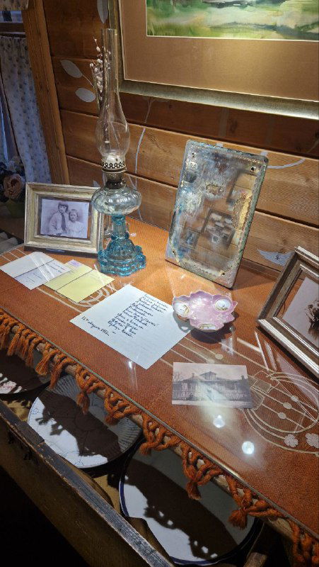 Витрина с предметами быта: лампа, рамки и мелкие вещи на покрытом тканью столе в деревянном интерьере музейного зала