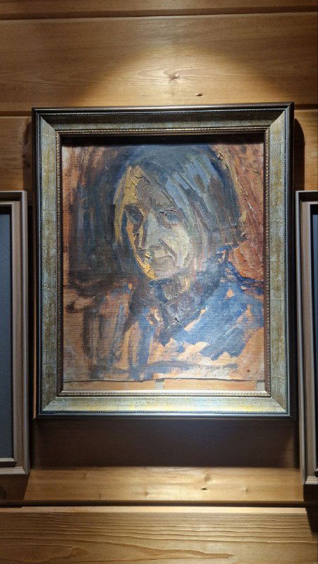 Портретная картина в рамке на деревянной стене музейного зала; масляный портрет в тёплой палитре на фоне бревенчатой комнаты