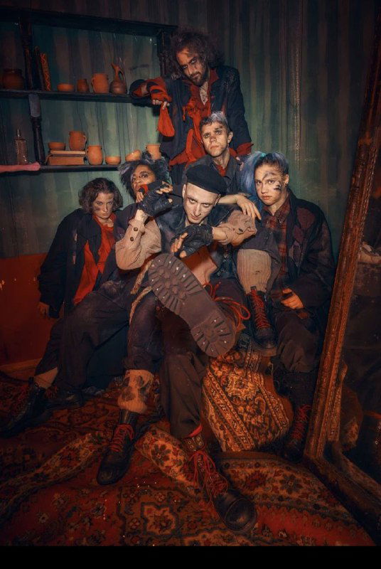 Группа актёров в костюмах крыс и других персонажей собирается в уютном тёмном уголке — коллективная сценическая фотография с характерными лицами и позами.