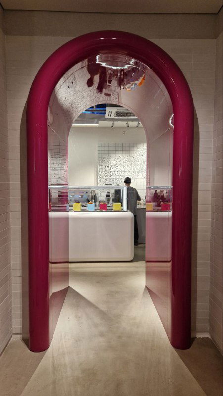 Проход в кафе Popmeal и барную стойку за аркой: яркая розовая арка ведёт в зону с прилавком и кофейной стойкой в современном пространстве подвала.