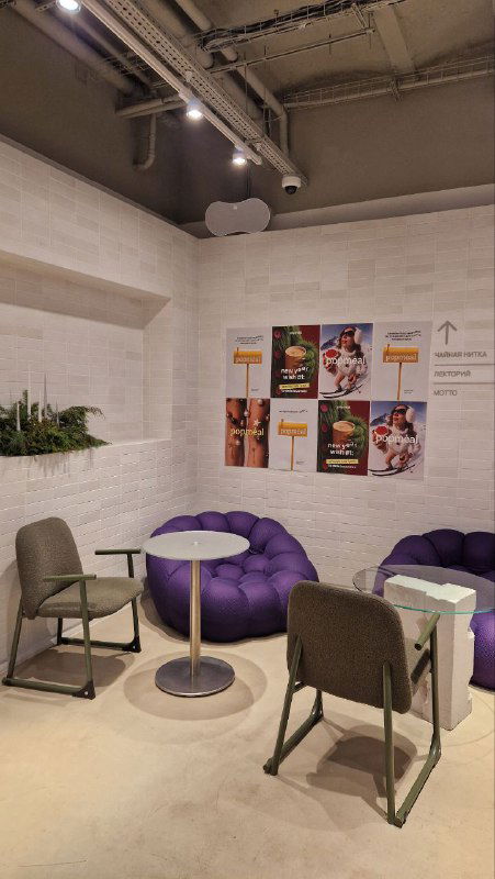 Уютный лаунж с мягкими пуфиками и плакатами на стене: небольшая зона для ожидания и общения в пастельных тонах внутри мультифункционального пространства.