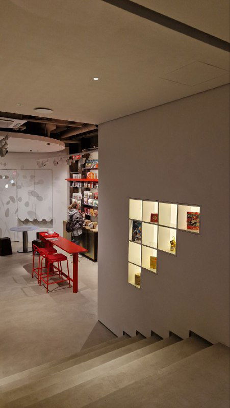 Вид с лестницы вниз: открытие уровня с витриной и полками, ступени ведут в нижнюю часть пространства, подчёркивая его многоуровневую планировку.