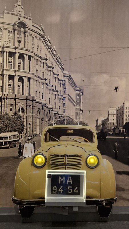 Стена экспозиции с чёрно‑белой фотографией улицы и жёлтым ретро‑автомобилем в оформлении, тематическая инсталляция, отражающая эпоху и поездки Прокофьева.