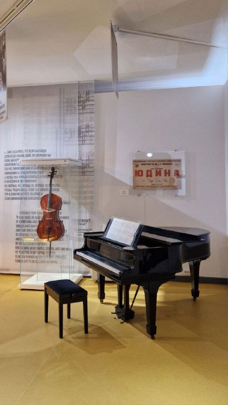 Зал с роялем и инструментами в музее Прокофьева: фортепиано, стул и текстовые панели, представляющие музыкальные аспекты жизни композитора.