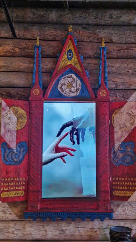 Декоративное зеркало в деревянной резной раме с народной росписью и современным визуальным элементом рук — сочетание фольклора и модерна в интерьере.