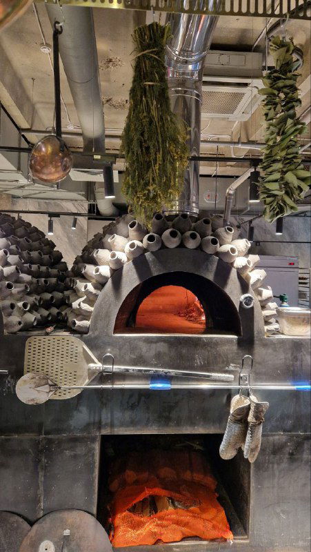 Каменная печь в открытой кухне ресторана «Чудо-Юдо»: рабочая зона с дровяной печью и аксессуарами для выпечки, промышленный открытый интерьер.