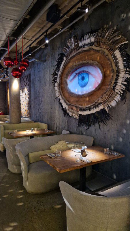 Атмосферный уголок зала с большим настенным арт‑объектом в виде глаза, мягкими диванами и приглушённым освещением — художественная сцена интерьера.