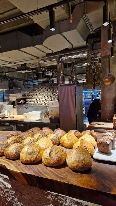 Хлебная доска: множество свежих круглых буханок на деревянной витрине; вид отделения пекарни внутри ресторана и крупный план выпечки.