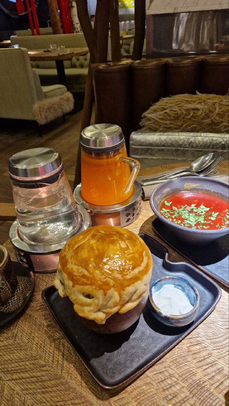 Подача супа в хлебной чаше с соусом и дополнительными сервировочными элементами на деревянном подносе — традиционная и эффектная подача блюда.