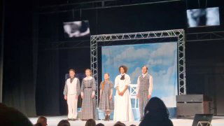 Актёры на сцене спектакля «ва-ва» во время поклона на фоне светлого декора и экранов; видна структура сцены и расположение исполнителей.