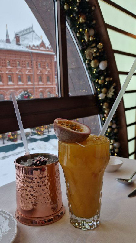 Два коктейля на столе в Peshi: один в медной кружке, второй в высоком стакане с фруктовой подачей — праздничные и авторские напитки.