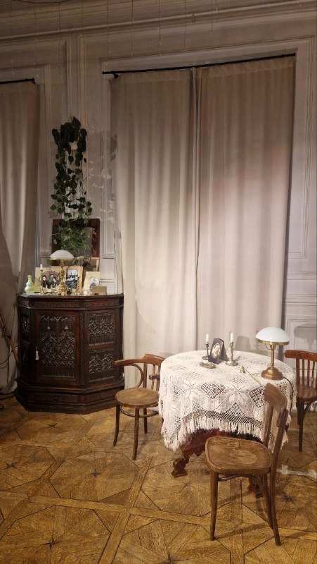 Кухонный или столовый уголок XVIII‑векового интерьера с кружевной скатертью, ретро‑предметами и старинным паркетом — сценическая бытовая деталь.