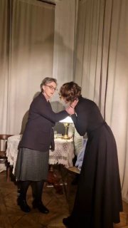 Интимный кадр рукопожатия или поддержки между двумя героинями на фоне антикварной мебели и лампы — театральный момент близости и драмы.