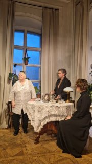 Трое актёров у круглого столика и фигура у окна: композиция сцены показывает связь прошлого и настоящего в постановке Наталии Мошиной по мотивам Чехова.