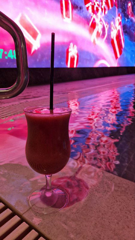 Коктейль у бортика бассейна GREMM: стакан с напитком на фоне большого экрана и цветной подсветки воды в зоне бара прямо в бассейне.