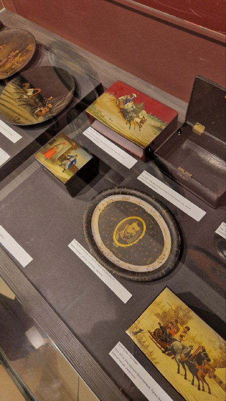 Витрина музея с коллекцией расписных шкатулок и подносов, экспонаты с подписями и подплечниками для экспозиции.