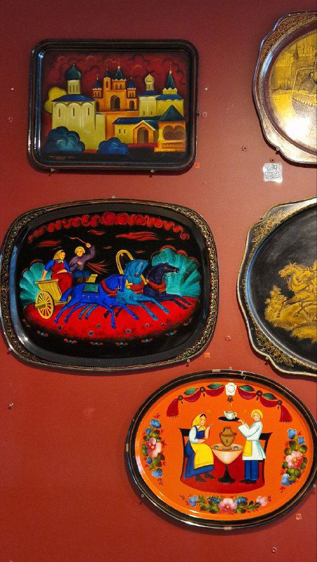 Стена с современными и старинными жостовскими подносами разной формы и размеров, пример стилистики росписи.