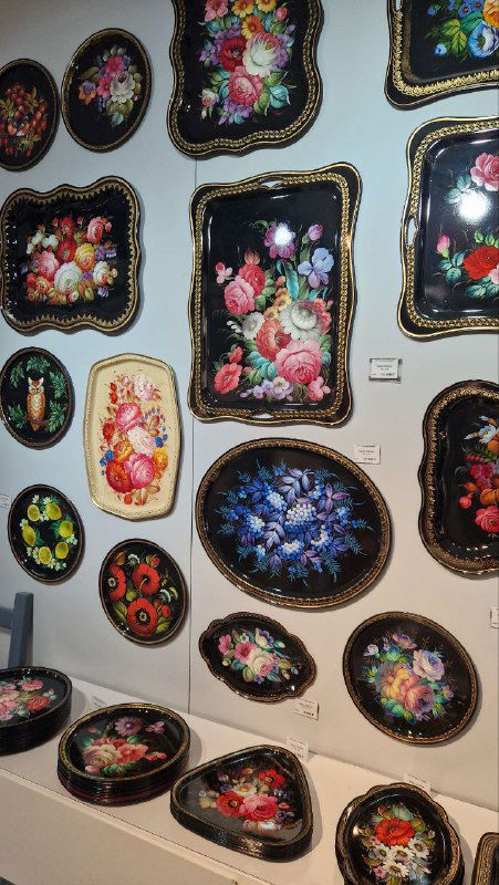 Стена с многочисленными образцами жостовских подносов разной формы и размеров, демонстрация разнообразия росписи и стилей.