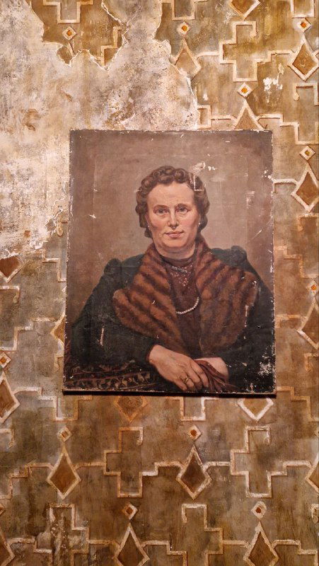 Фрагмент стены ресторана с портретом в рамке и состаренной декоративной отделкой, создающей атмосферу XIX века и художественную потертость.