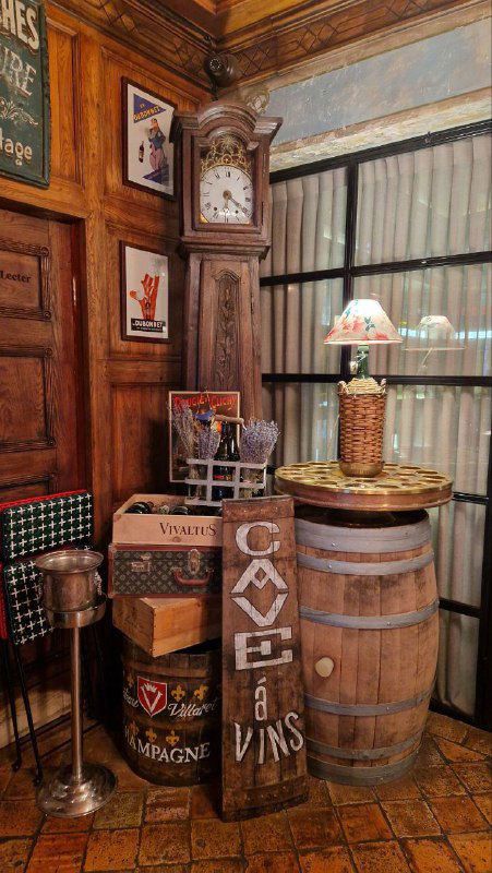 Уютная зона ресторана с деревянными бочонками, табличками на английском и французском, полками с винными аксессуарами и тёплой лампой.