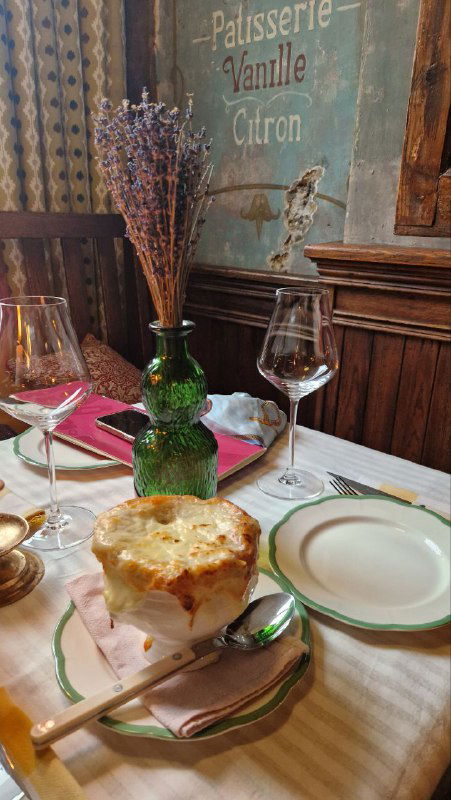 Тарелка с луковым супом в супнице на столе: поджаренная корочка и сервировка в винтажной посуде, рядом бокал и веточка лаванды в вазе.