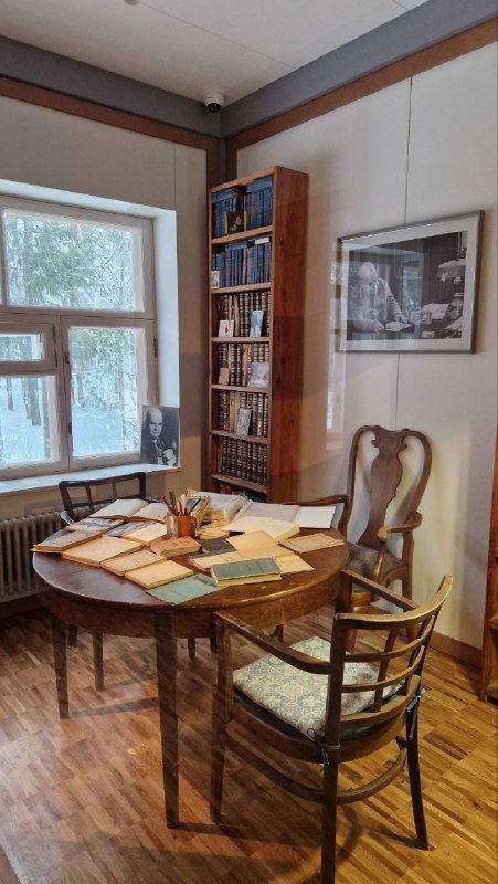 Круглый стол с разбросанными письмами, книгами и бумажными объектами на фоне окон — часть экспозиции переписок и дневников в музее.