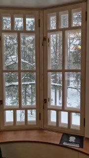 Большое окно-эркер коттеджа с видом на заснеженный сад Переделкино, через которое в экспозицию проникает холодный дневной свет.
