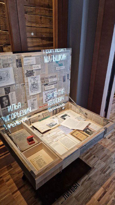 Витрина с архивными материалами и подсветкой: коробки, письма и сокращённые подписи, демонстрирующие документальную основу выставки.